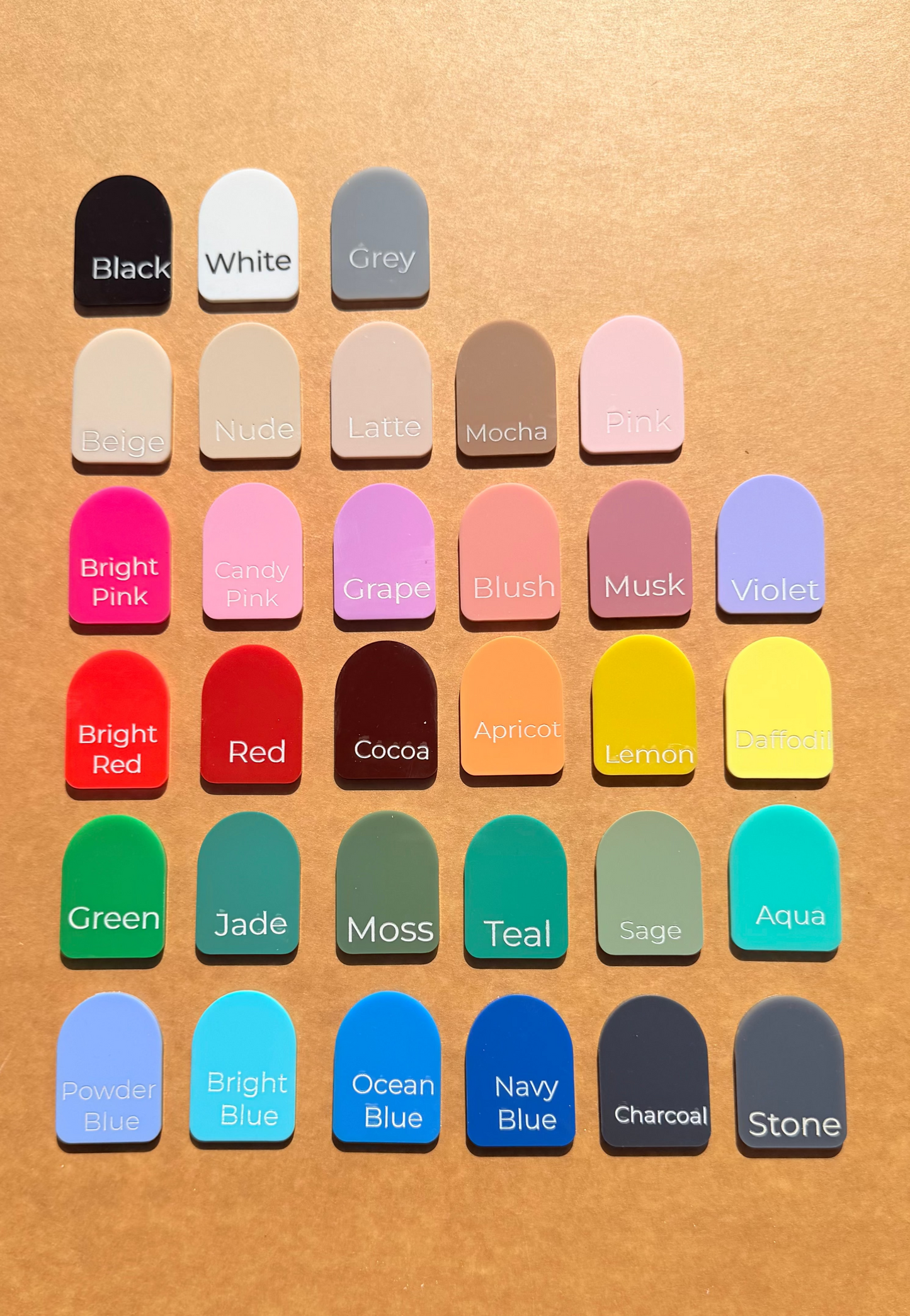 A grid of 30  colour swatches labeled with names like Black, White, Grey, Pink, Red, Green, Blue, and Stone, arranged on a warm tan textured background.